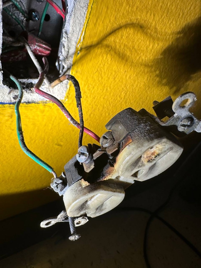 Real service call photo: Melted, charred electrical outlet pulled from a wall with burnt wire insulation by KiloWire Electric